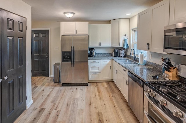 kitchen featuring white cabinetry, sink, dark stone counters, stainless steel appliances, and light wood-type flooring