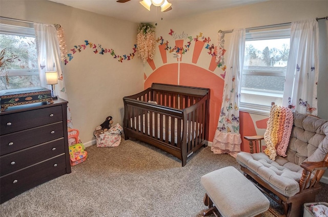 carpeted bedroom featuring multiple windows, a crib, and ceiling fan