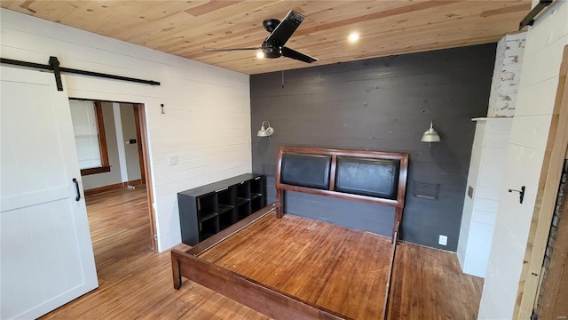 interior space with ceiling fan, a barn door, wooden ceiling, and light hardwood / wood-style floors