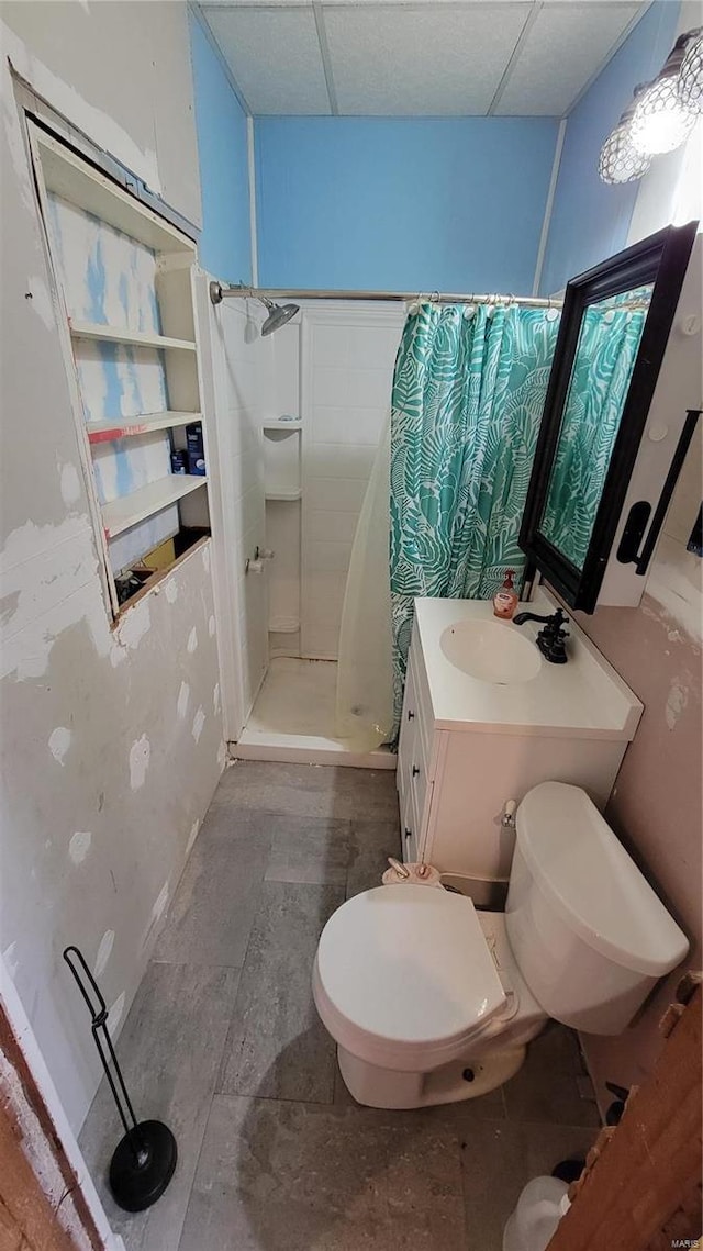 bathroom featuring toilet, a drop ceiling, vanity, and walk in shower