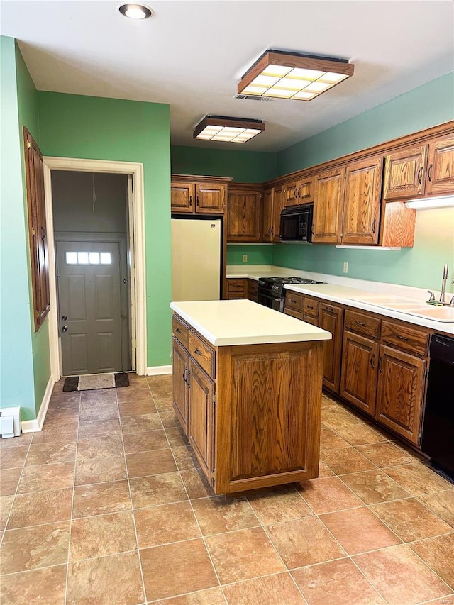 kitchen featuring light countertops, a kitchen island, a sink, black appliances, and baseboards