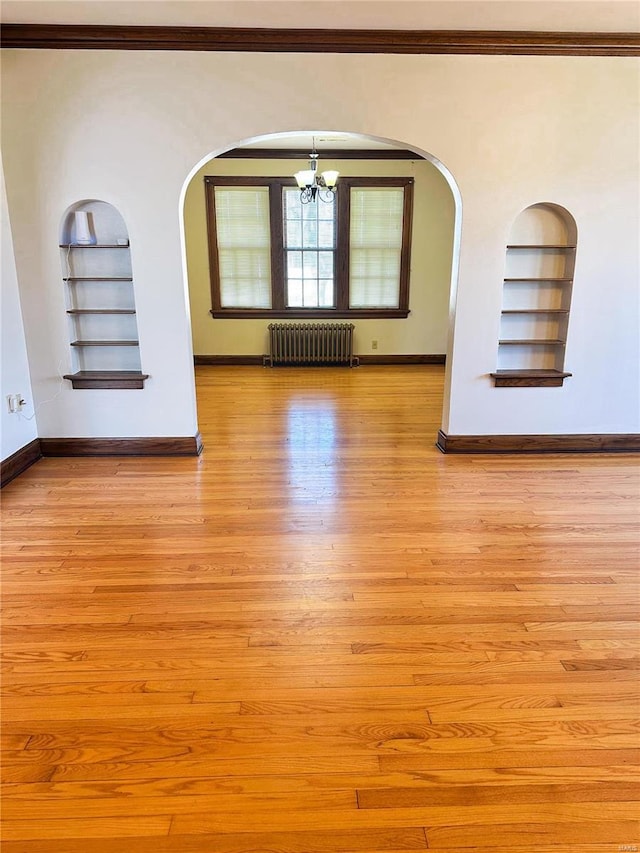 unfurnished room featuring baseboards, built in shelves, light wood-type flooring, and radiator