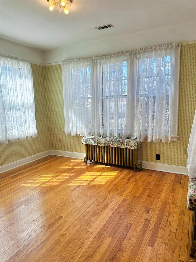 unfurnished room with wood finished floors, visible vents, baseboards, radiator heating unit, and wallpapered walls