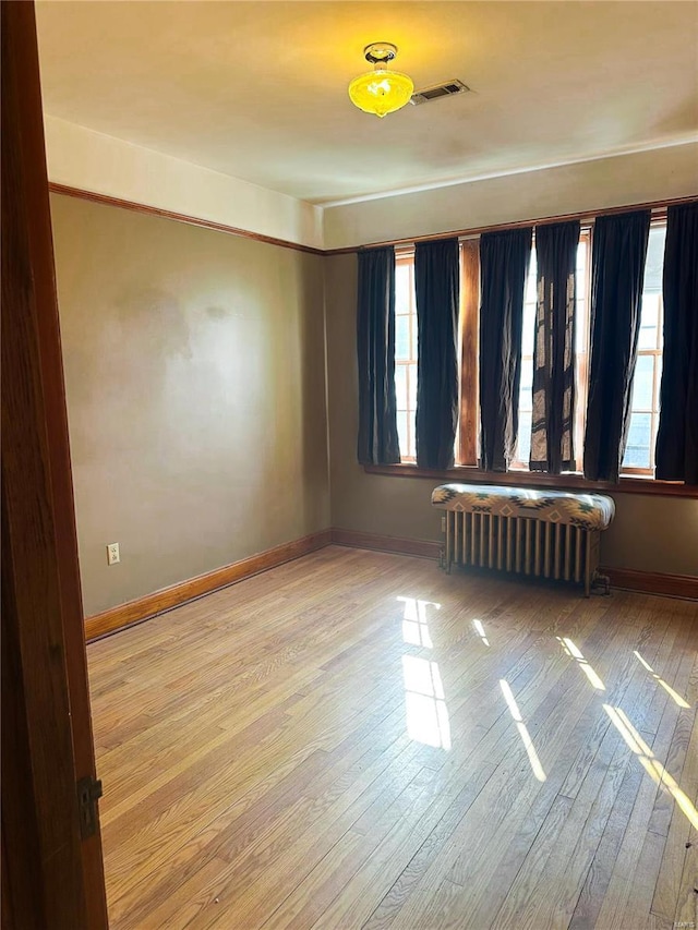 empty room with radiator, baseboards, and wood finished floors