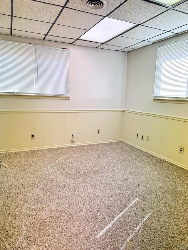 unfurnished room featuring carpet floors, wainscoting, visible vents, and a drop ceiling