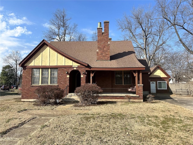 tudor house with a shingled roof, a chimney, a porch, a front lawn, and brick siding