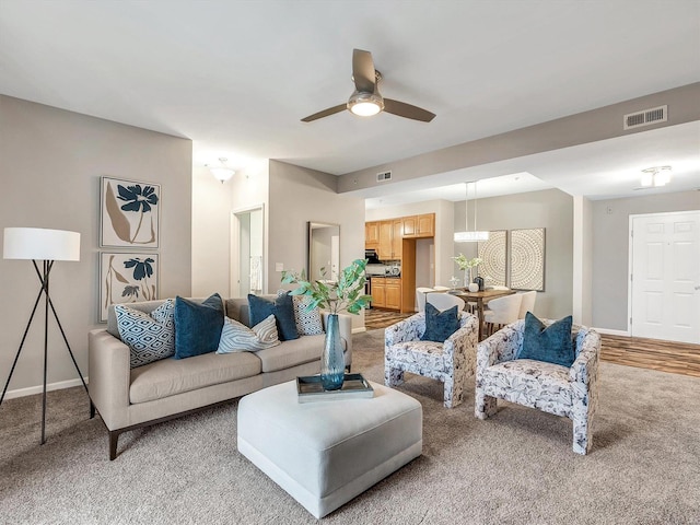 living area with a ceiling fan, visible vents, light carpet, and baseboards