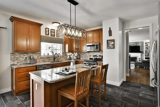 kitchen featuring stainless steel appliances, a center island, light stone countertops, sink, and pendant lighting