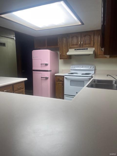 kitchen with light countertops, visible vents, a sink, white appliances, and under cabinet range hood