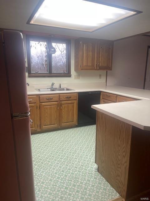 kitchen with black dishwasher, brown cabinets, freestanding refrigerator, light floors, and a sink