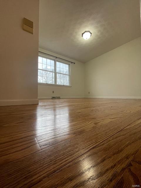 spare room featuring visible vents, baseboards, vaulted ceiling, and wood finished floors