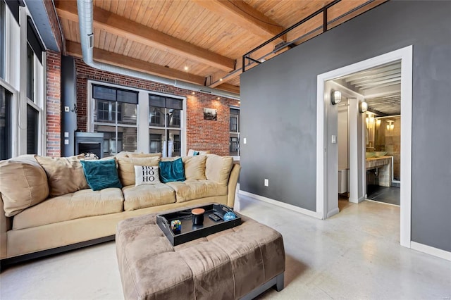 living area featuring brick wall, finished concrete flooring, baseboards, beamed ceiling, and wood ceiling