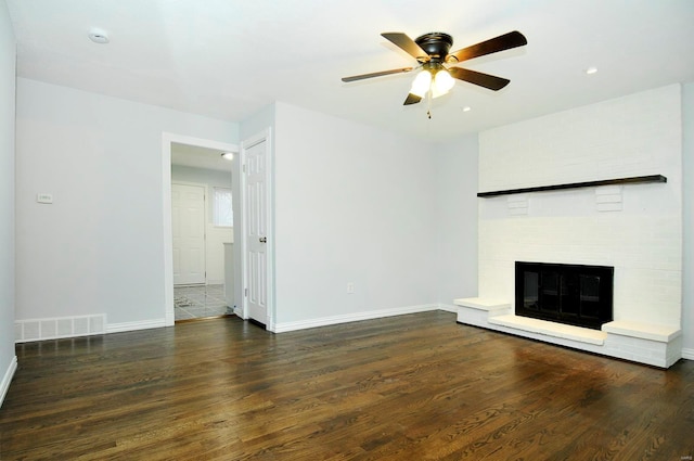 unfurnished living room featuring a brick fireplace, dark wood-type flooring, and ceiling fan