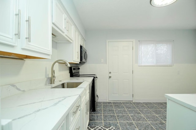 kitchen featuring sink, tile walls, white cabinets, stainless steel appliances, and light stone countertops