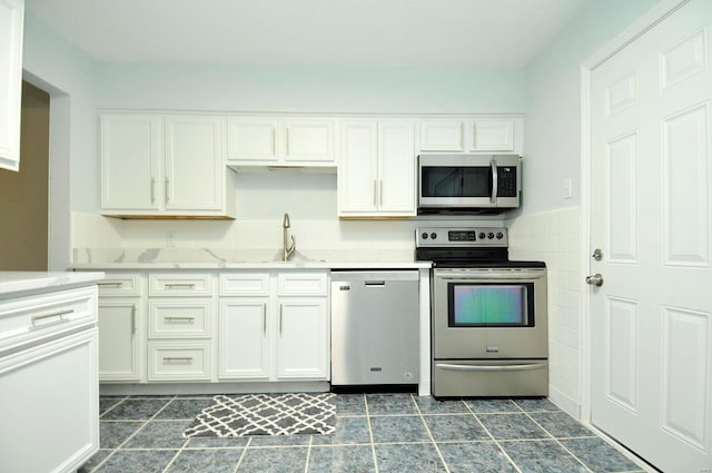 kitchen with white cabinetry, sink, stainless steel appliances, and tile walls