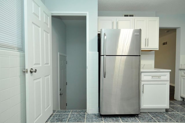 kitchen with a textured ceiling, stainless steel fridge, and white cabinets