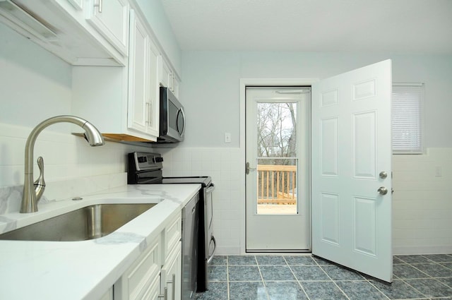 kitchen featuring appliances with stainless steel finishes, sink, tile walls, white cabinets, and dark tile patterned flooring