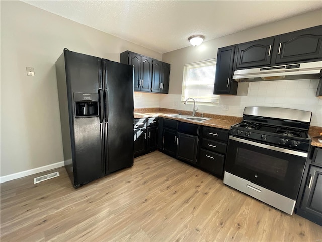 kitchen with sink, backsplash, stainless steel gas range oven, light hardwood / wood-style floors, and black fridge