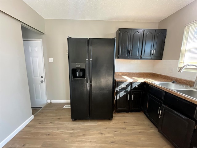 kitchen with sink, decorative backsplash, black fridge with ice dispenser, and light wood-type flooring