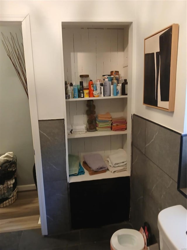 bathroom featuring wood-type flooring, toilet, and tile walls