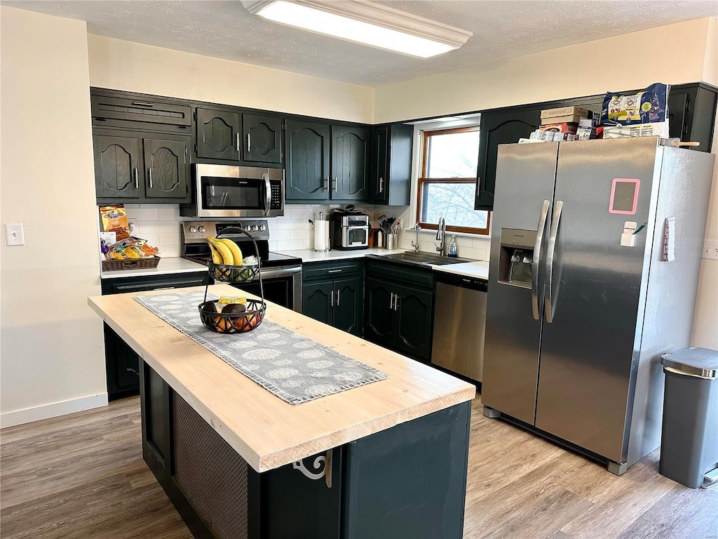 kitchen with sink, tasteful backsplash, a center island, light wood-type flooring, and appliances with stainless steel finishes