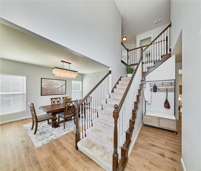 staircase with a chandelier, baseboards, a high ceiling, and wood finished floors