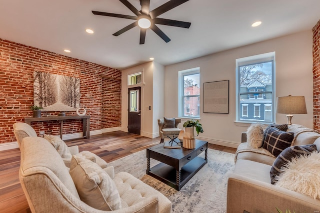 living room featuring hardwood / wood-style floors, ceiling fan, and brick wall