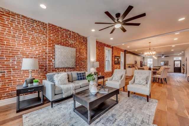 living room featuring ceiling fan with notable chandelier, light wood-type flooring, and brick wall