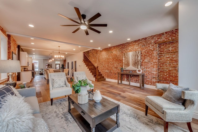 living room featuring ceiling fan with notable chandelier, light hardwood / wood-style flooring, and brick wall