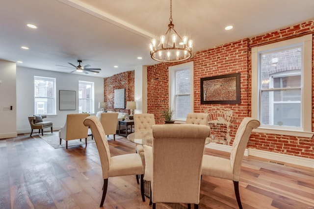 dining area featuring hardwood / wood-style flooring, brick wall, and ceiling fan with notable chandelier