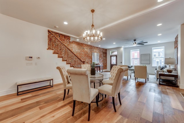 dining space with ceiling fan with notable chandelier, brick wall, and light hardwood / wood-style floors