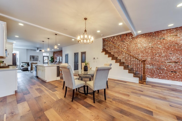 dining space featuring brick wall, ceiling fan with notable chandelier, sink, beam ceiling, and light hardwood / wood-style flooring