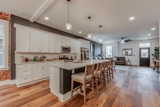 kitchen with appliances with stainless steel finishes, pendant lighting, white cabinetry, sink, and a center island with sink