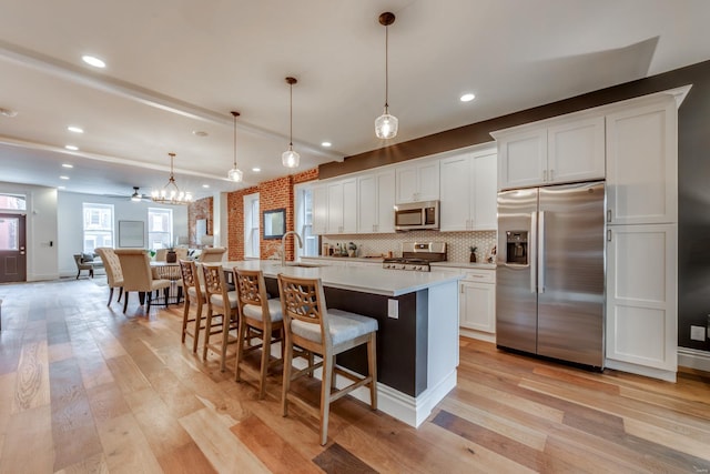 kitchen featuring stainless steel appliances, white cabinetry, an island with sink, and decorative light fixtures