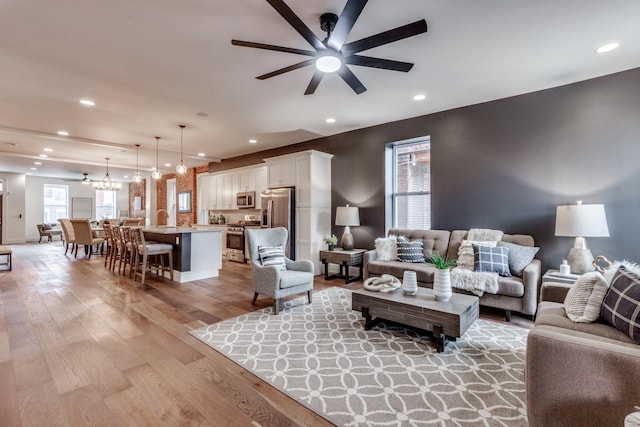 living room with ceiling fan with notable chandelier, a wealth of natural light, and light hardwood / wood-style flooring