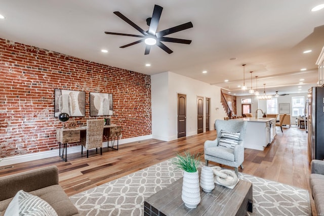 living room with brick wall, sink, ceiling fan, and light hardwood / wood-style flooring