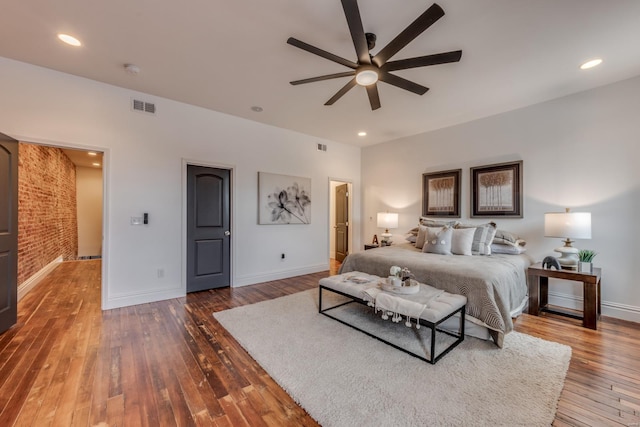 bedroom featuring wood-type flooring, ceiling fan, and brick wall