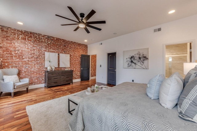 bedroom featuring ceiling fan, brick wall, ensuite bathroom, and hardwood / wood-style floors