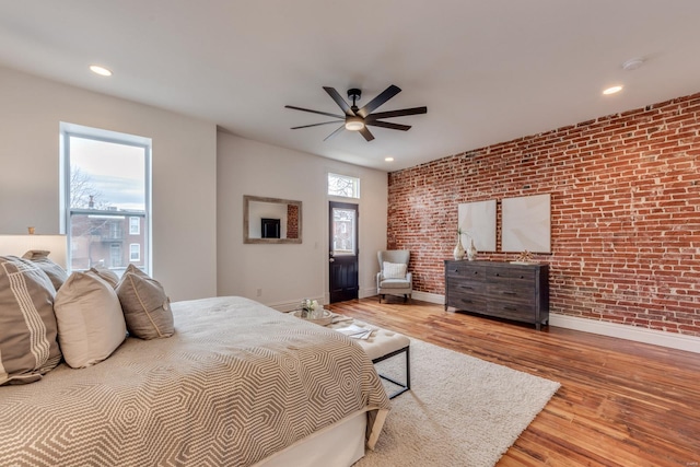 bedroom with hardwood / wood-style floors, ceiling fan, and brick wall