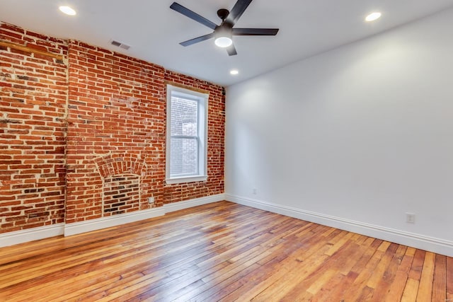 spare room with ceiling fan, brick wall, and light wood-type flooring