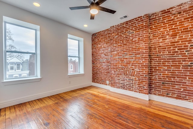 unfurnished room with wood-type flooring, brick wall, and ceiling fan