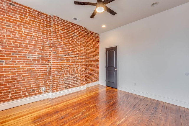 empty room with light hardwood / wood-style floors, ceiling fan, and brick wall