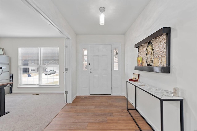 foyer featuring light wood-style flooring, baseboards, and light colored carpet