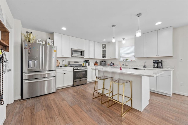 kitchen with decorative light fixtures, white cabinetry, a center island, stainless steel appliances, and light wood-type flooring