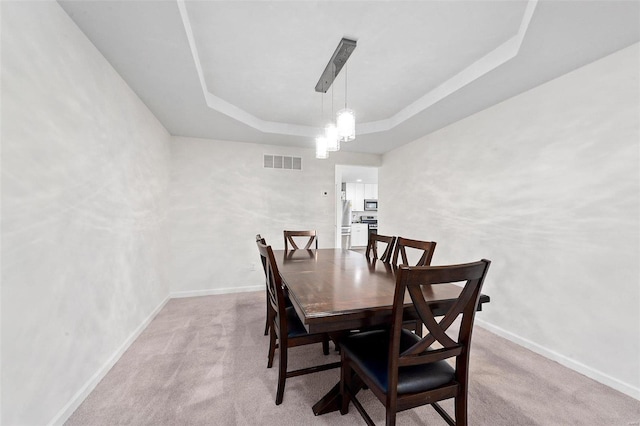 carpeted dining area with a raised ceiling