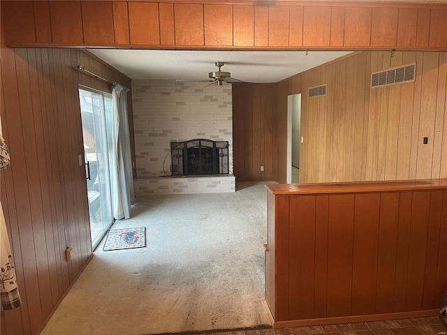 unfurnished living room featuring a brick fireplace, wooden walls, ceiling fan, and carpet