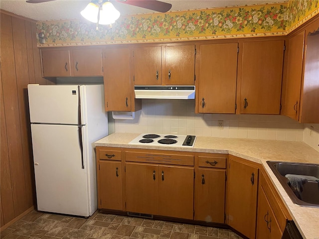 kitchen with sink, white appliances, ceiling fan, wooden walls, and decorative backsplash