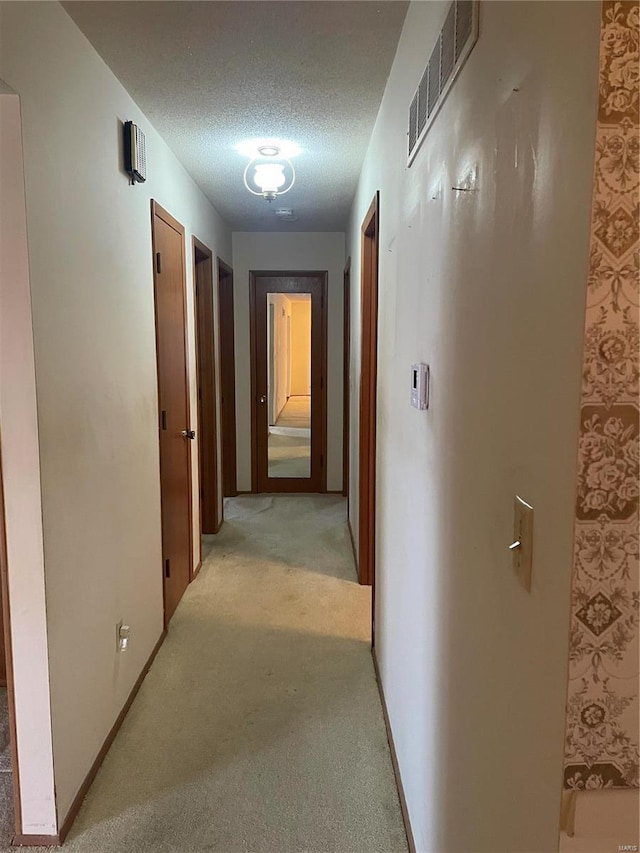 hallway featuring light carpet and a textured ceiling