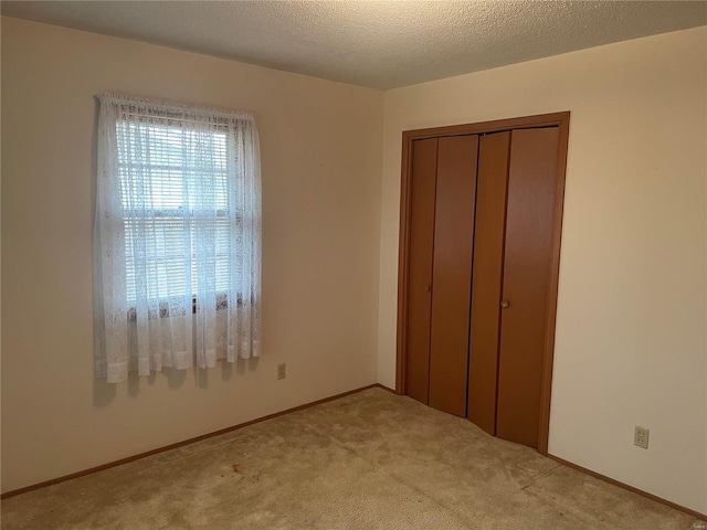 unfurnished bedroom featuring light carpet, a textured ceiling, and a closet