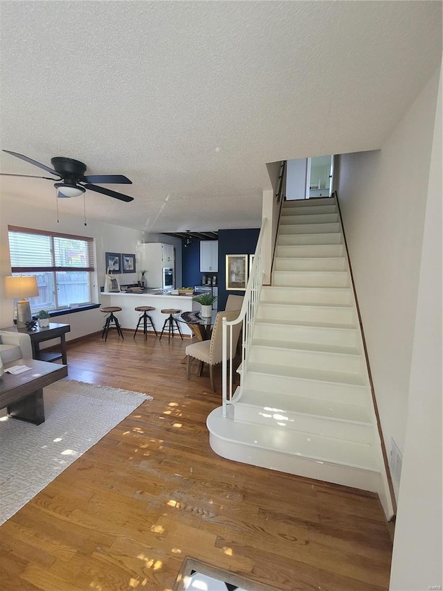 staircase with hardwood / wood-style flooring, ceiling fan, and a textured ceiling